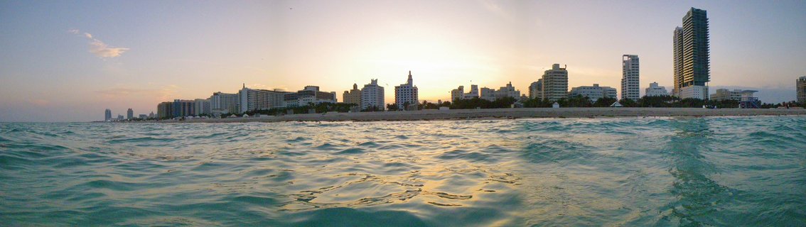 Panoramic view of Miami Beach skyline from the ocean at sunset with high-rise buildings along the shoreline and waves in the foreground