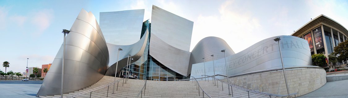 Wide view of Walt Disney Concert Hall showing curved stainless steel panels and stone staircase under blue sky in Downtown Los Angeles