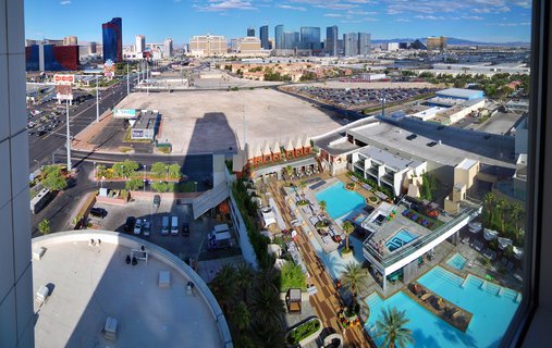 Aerial photograph showing multiple swimming pools with palm trees at a Las Vegas resort, with casino hotels and city skyline visible in the background under blue sky