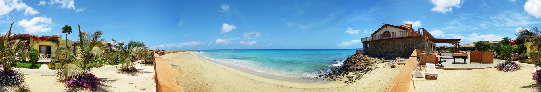 Beach resort in Sal, Cape Verde showing turquoise ocean water, sandy beach, palm trees, and coastal buildings under blue sky