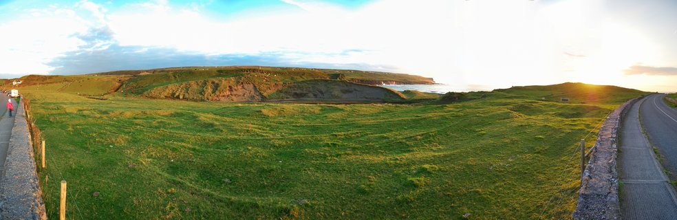 Panoramic view of green coastal grassland with stone walls, cliffs, and Atlantic Ocean at sunset near Doolin, Ireland