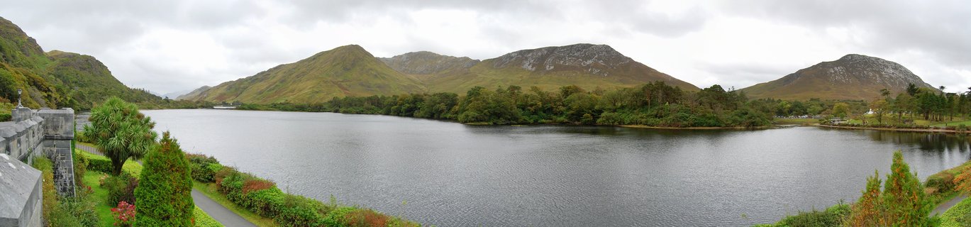 Wide landscape showing a calm lake surrounded by green mountains under cloudy sky in Connemara, Ireland