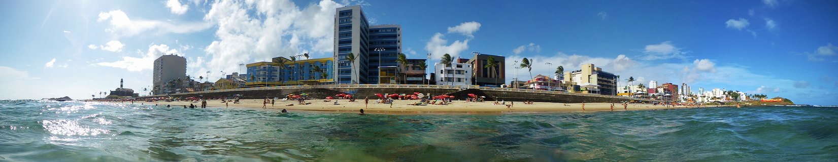 Beachgoers enjoy Porto da Barra Beach with Farol da Barra lighthouse and Salvador cityscape in Bahia, Brazil