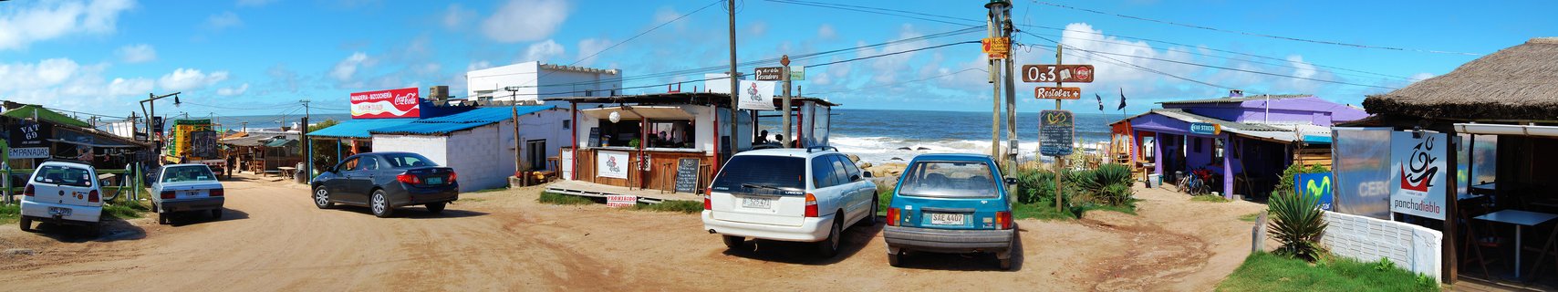 Street scene showing colorful beachfront buildings, parked cars, and ocean view in Punta del Diablo, Uruguay