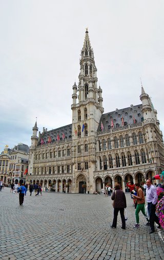 Ornate Gothic town hall building with tall decorative spire and arched windows on cobblestone square with people walking