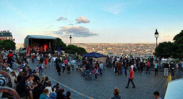 Outdoor concert crowd gathers at Montmartre overlooking Paris cityscape at sunset