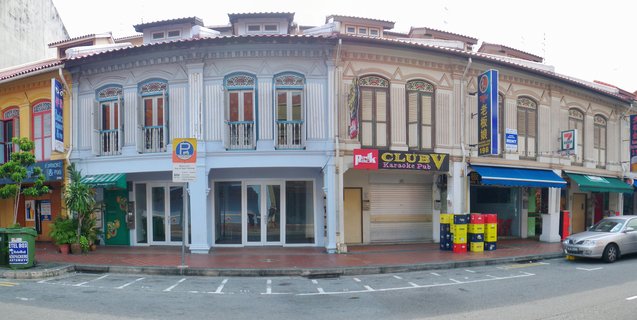 Street view of colorful two-story heritage shophouses in Singapore with ornate architectural details, commercial signage, and parked car