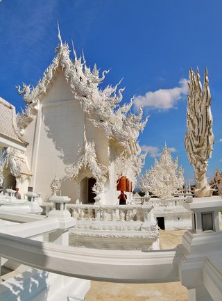 Ornate white Buddhist temple with intricate carved details, decorative roof elements, and traditional Thai architecture against blue sky