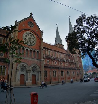Red brick Gothic cathedral with twin spires and crosses, arched windows, rose window, motorbikes on street, Ho Chi Minh City Vietnam