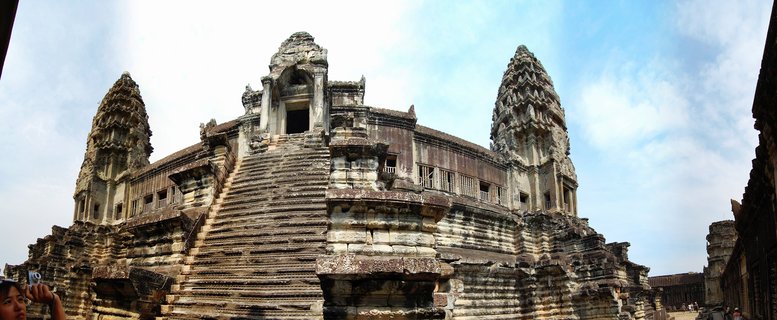 Ancient stone temple towers of Angkor Wat with steep staircase leading to central structure under blue sky with scattered clouds