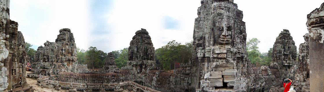 Multiple ancient stone temple towers with carved faces at Bayon Temple in Cambodia, with overcast sky and green trees in background