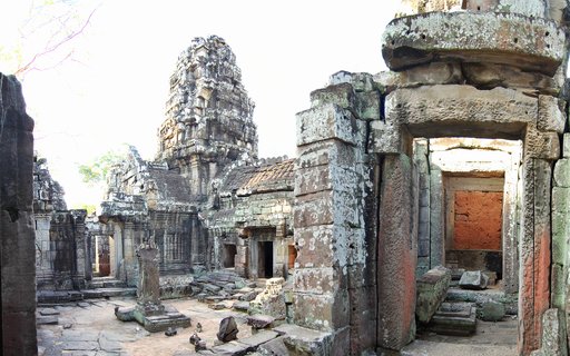 Ancient stone temple ruins showing weathered sandstone blocks, a central tower structure, and multiple doorways at Angkor Wat in Cambodia