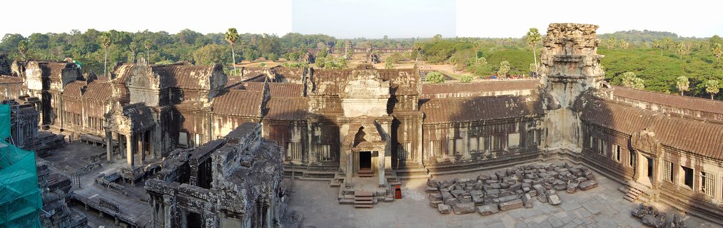 Aerial view of ancient stone temple complex with multiple towers, galleries, and courtyards surrounded by green tropical forest