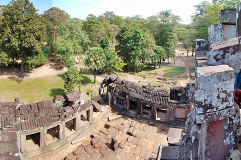 High-angle view of ancient stone temple ruins with collapsed roof sections, surrounded by green tropical trees and forest at Angkor Wat, Cambodia