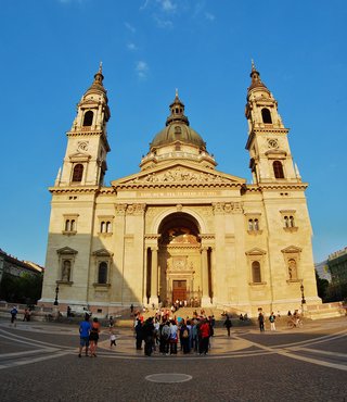 St. Stephen's Basilica in Budapest with two bell towers and central dome, tourists on cobblestone plaza, clear blue sky