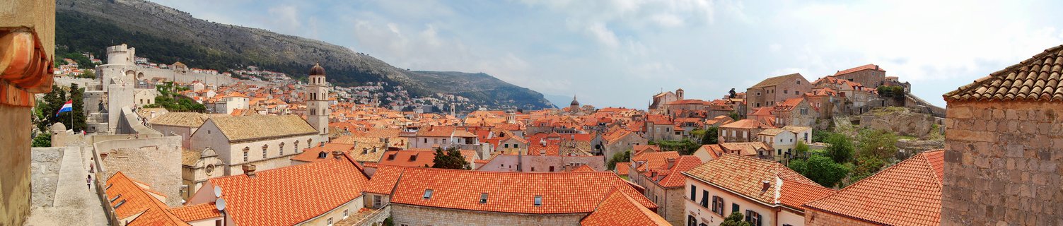 Panoramic view of Dubrovnik Old Town showing dense cluster of orange terracotta rooftops, stone buildings, church bell towers, and surrounding medieval walls with hills in background