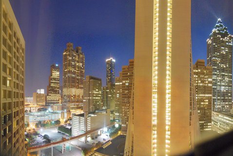 Night photograph of Atlanta skyline showing multiple illuminated high-rise buildings against deep blue sky with elevated transit track and parking structure visible in foreground