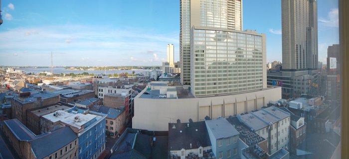 Panoramic cityscape of New Orleans showing modern high-rise buildings and historic brick structures with the Mississippi River in the distance under a blue sky
