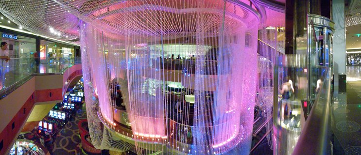 Casino interior with large purple fiber optic light installation, slot machines, glass elevator, and multi-level gaming floor in Las Vegas
