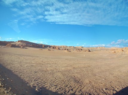 Desert landscape showing eroded rock formations and sand dunes under blue sky with wispy clouds in the Atacama Desert, Chile