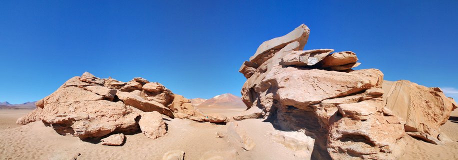 Large wind-eroded sandstone rock formations in a barren desert landscape under clear blue sky with distant mountains