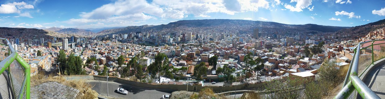 Panoramic cityscape of La Paz, Bolivia showing dense urban buildings in a mountain valley with blue sky and clouds above