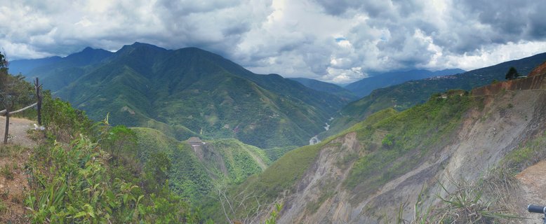 Panoramic view of green mountain valleys with steep slopes, a river in the distance, and cloudy sky over the Andes near La Paz, Bolivia
