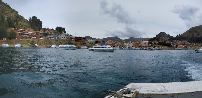 White tourist boats on Lake Titicaca waters with colorful hillside town buildings and mountains in background under cloudy sky
