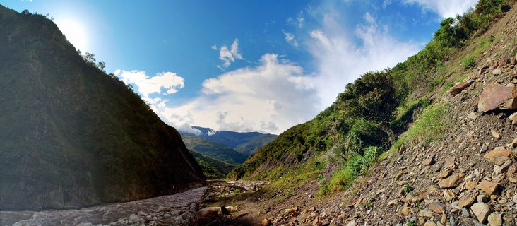 Wide mountain valley with river flowing between steep green-covered slopes under blue sky with clouds near Machu Picchu Peru