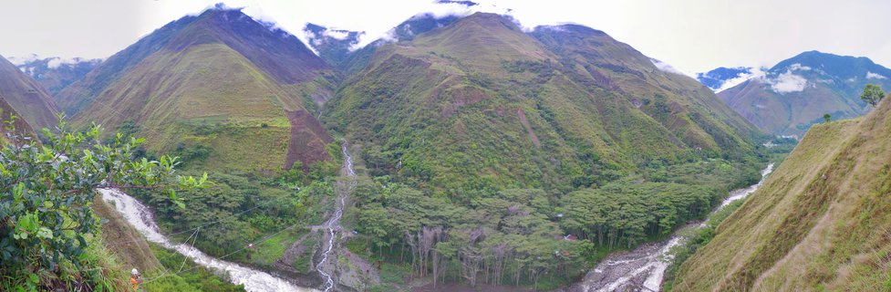 Green mountain valley in Peru with rivers flowing through dense forest and clouds around mountain peaks