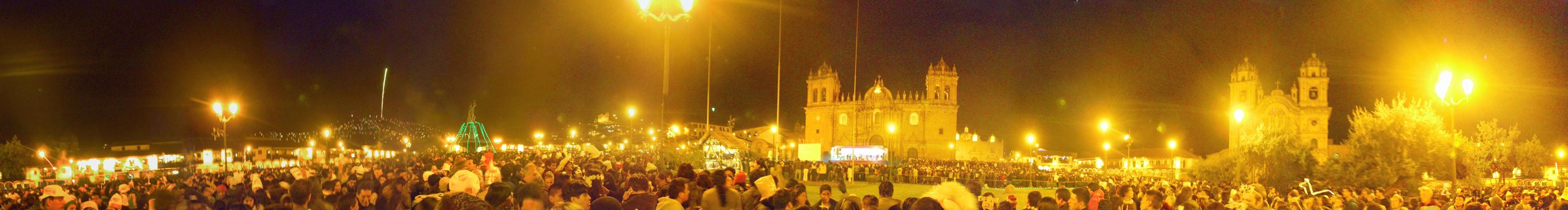 Large crowd gathered at night in a plaza with illuminated colonial cathedral buildings and street lights in Arequipa, Peru