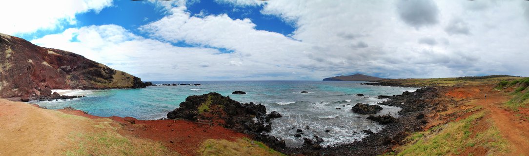 Panoramic coastal view of Easter Island showing red volcanic hills, black rock formations in turquoise water, and cloudy blue sky