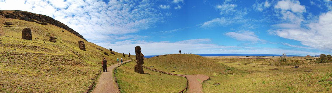 Multiple Moai stone statues on grassy volcanic hillside with walking paths and visitors, Easter Island, Chile