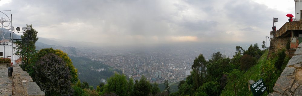 Panoramic view of Bogotá city from Monserrate hill showing urban sprawl under cloudy sky with stone walls and vegetation in foreground