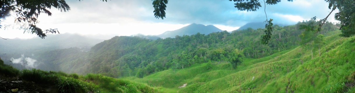 Panoramic view of green forested mountains with mist in valleys and cloudy sky over Sierra Nevada de Santa Marta in Colombia