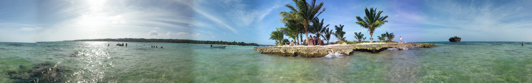 Small tropical island with palm trees in clear turquoise Caribbean water with people swimming nearby, San Andres, Colombia