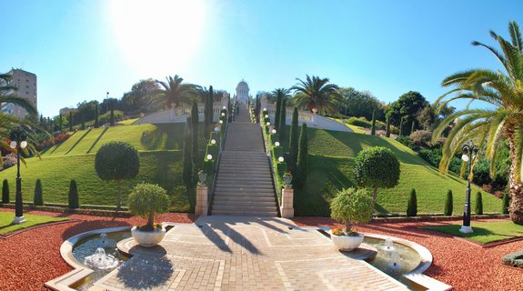 White domed Bahá'í shrine atop terraced gardens with staircases, fountains, palm trees and manicured lawns on Mount Carmel in Haifa, Israel under clear blue sky