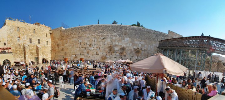 Large crowd of people praying at the Western Wall in Jerusalem, with ancient stone wall and clear blue sky
