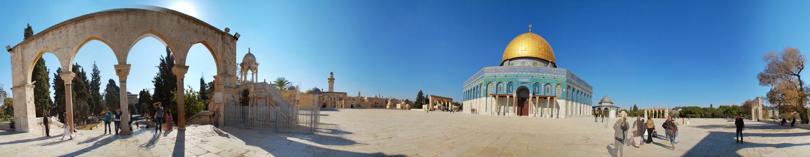 Panoramic view of the Dome of the Rock with its golden dome and blue-tiled walls on the Temple Mount plaza in Jerusalem, with stone archways and visitors visible under a clear blue sky