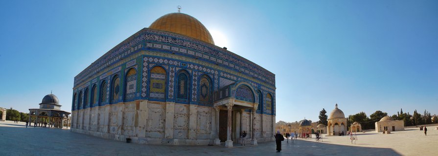The Dome of the Rock shrine with golden dome and blue tiled walls on Temple Mount plaza in Jerusalem with visitors walking under clear blue sky