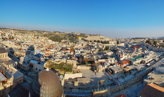 Aerial panoramic view of Jerusalem Old City showing the golden Dome of the Rock mosque surrounded by dense limestone buildings under clear blue sky