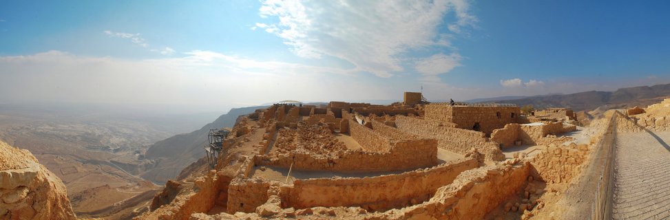 Panoramic view of ancient stone fortress ruins at Masada with desert valley and blue sky