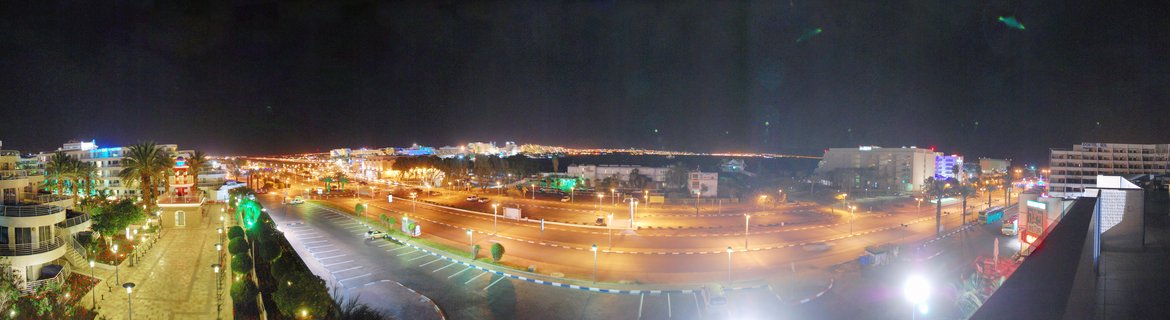 Night aerial view of Eilat, Israel showing illuminated streets, parking lots, hotels, palm trees, and urban buildings under dark sky