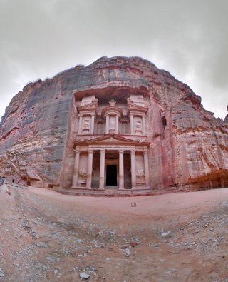 The Treasury monument at Petra, Jordan, carved into rose-red sandstone cliff with six columns and ornate pediments under overcast sky