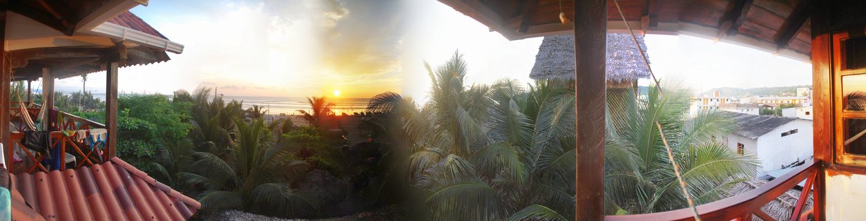 Sunset over ocean viewed from wooden terrace with palm trees and tropical buildings in Canoa, Ecuador