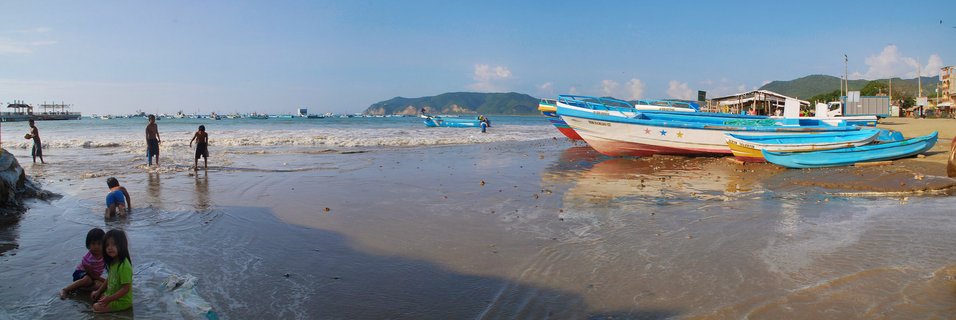 Colorful fishing boats beached on shore with children playing in shallow water, Puerto López, Ecuador