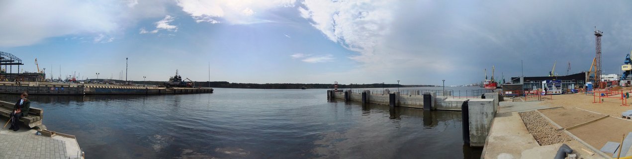 Panoramic view of Klaipeda seaport showing harbor water, concrete piers, yellow industrial cranes, construction site, and port buildings under partly cloudy sky