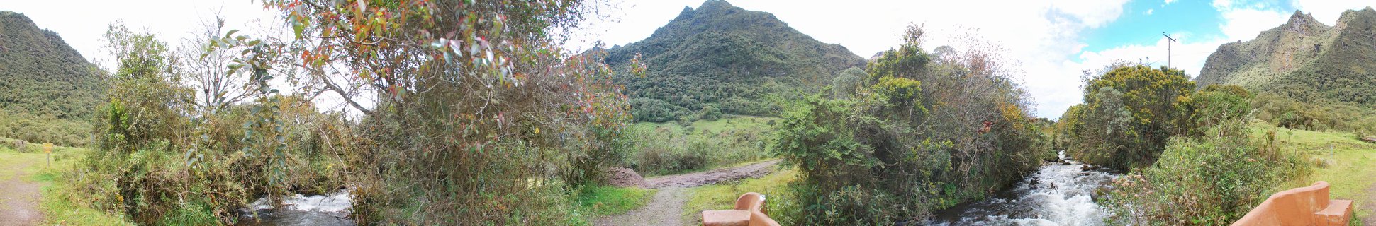 Wide landscape showing a river flowing through green mountains covered in dense rainforest vegetation in Tena, Ecuador