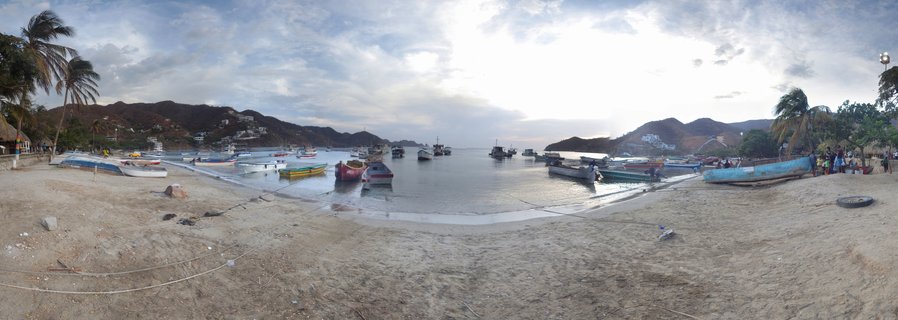 Fishing boats on sandy beach in a bay surrounded by hills and palm trees in Cartagena, Colombia