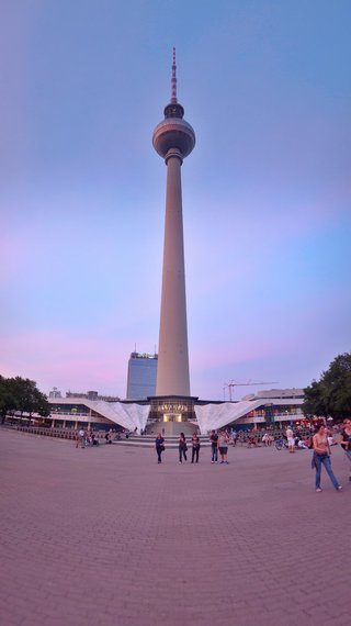 Berlin TV Tower (Fernsehturm) at Alexanderplatz with people walking on the plaza during evening twilight with purple and blue sky